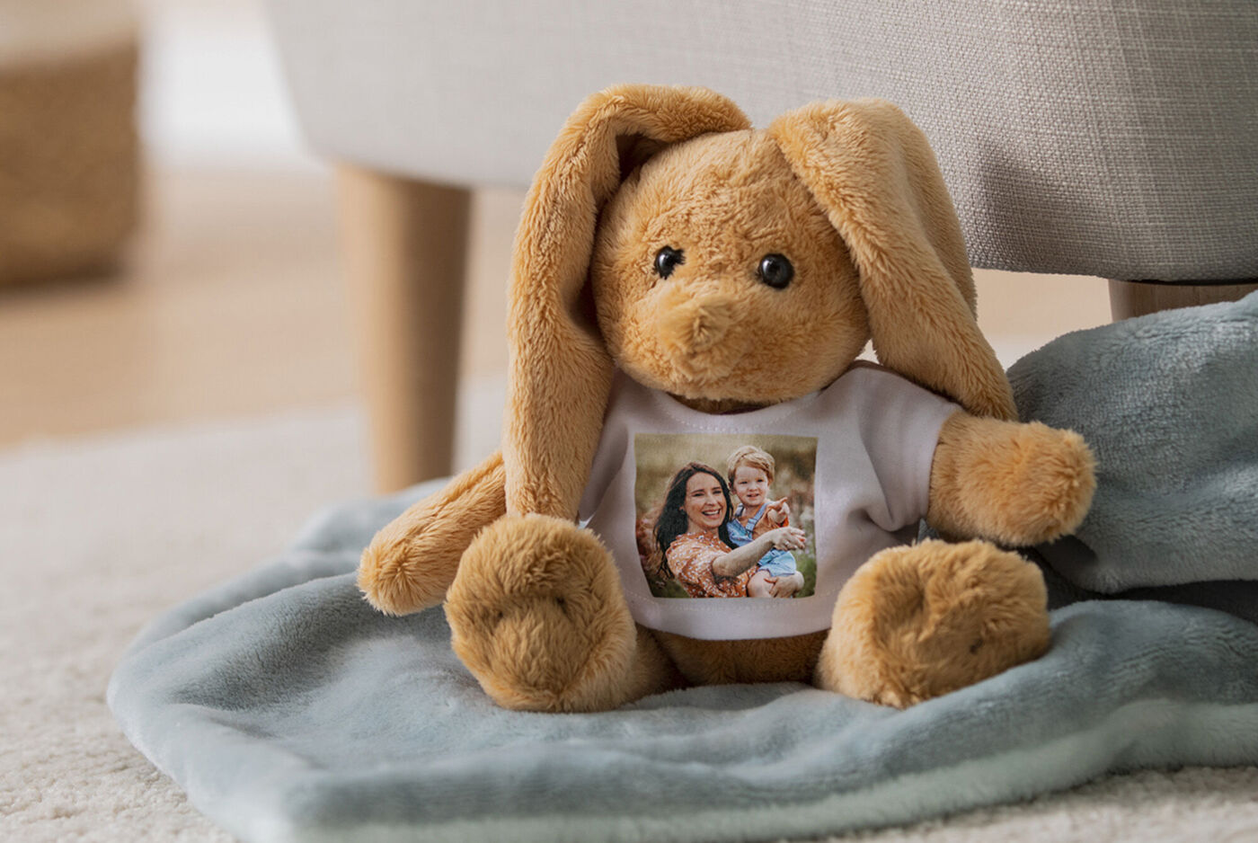 Un lapin en peluche mignon avec un t-shirt montrant une photo de deux personnes, assis sur une couverture douce.