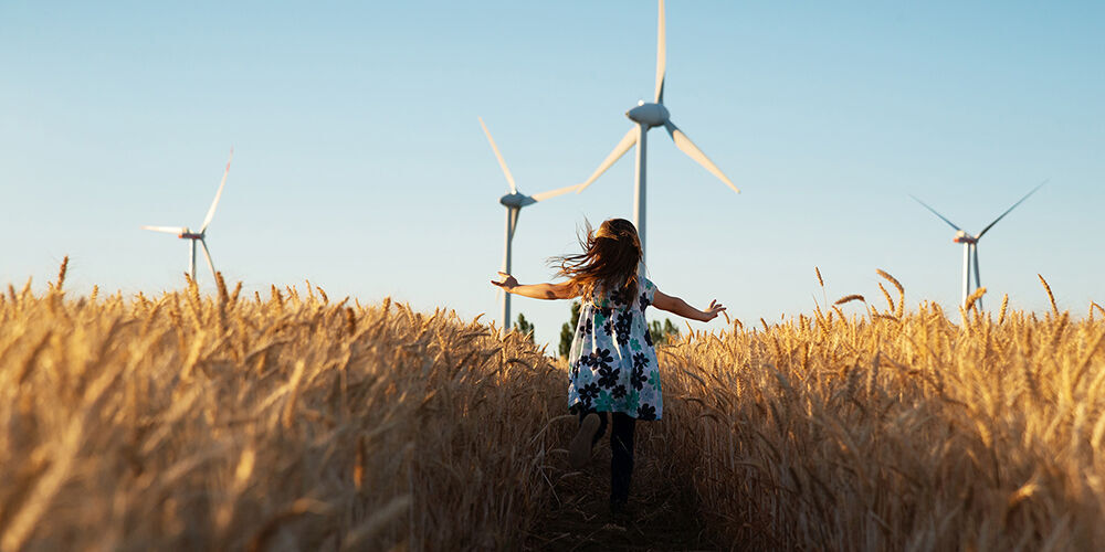 Une fille dans un champ fleuri avec des éoliennes en arrière-plan, observant joyeusement la nature.