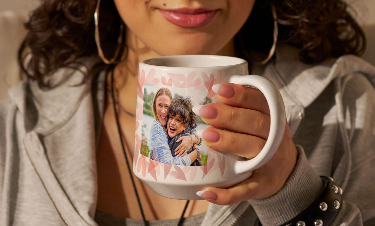 Une personne tient une tasse à café personnalisée avec une photo de deux personnes souriantes.