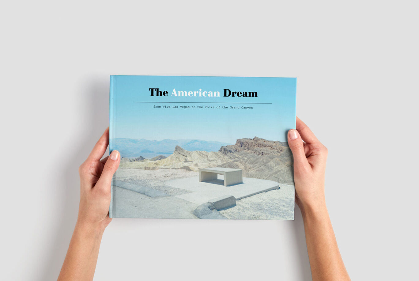 Une personne tient un CEWE FOTOBUCH intitulé 'The American Dream' devant un beau paysage.