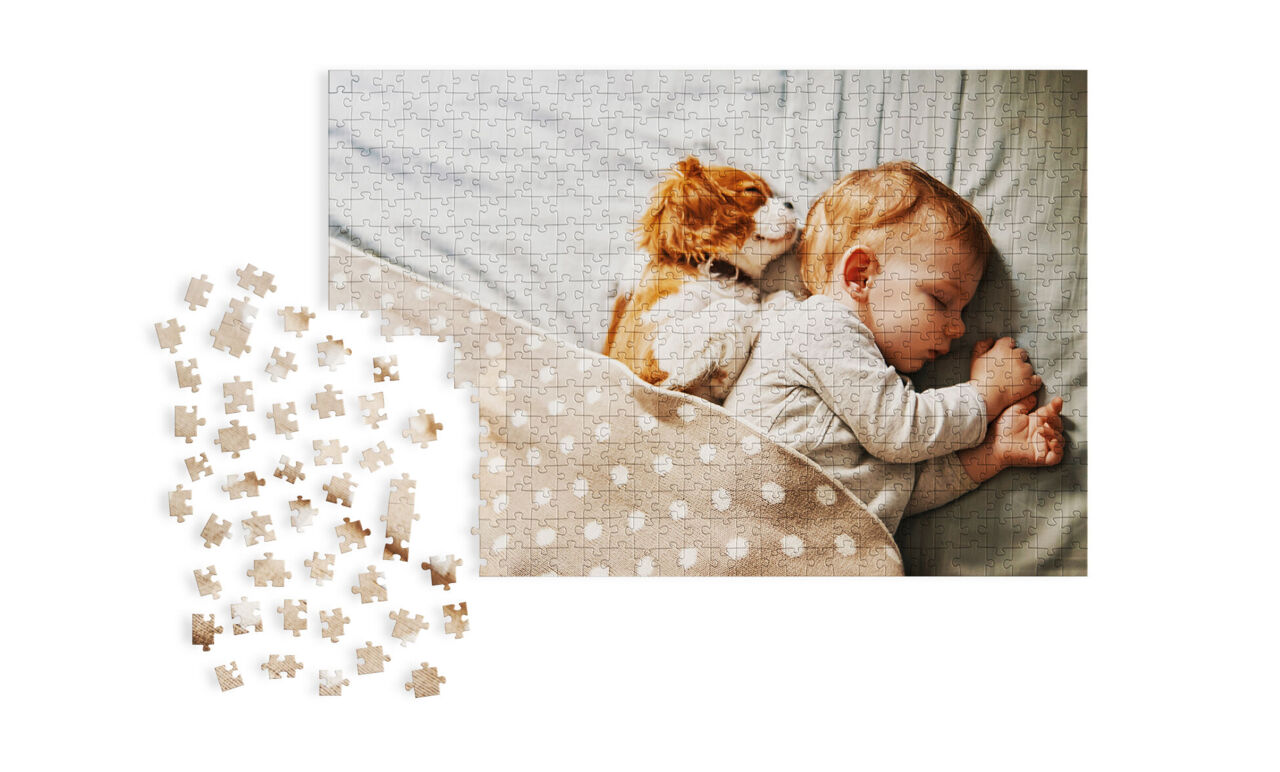 Een slapende baby ligt op bed omringd door een zachte, stippen hoes. Een hond knuffelt naast de baby.